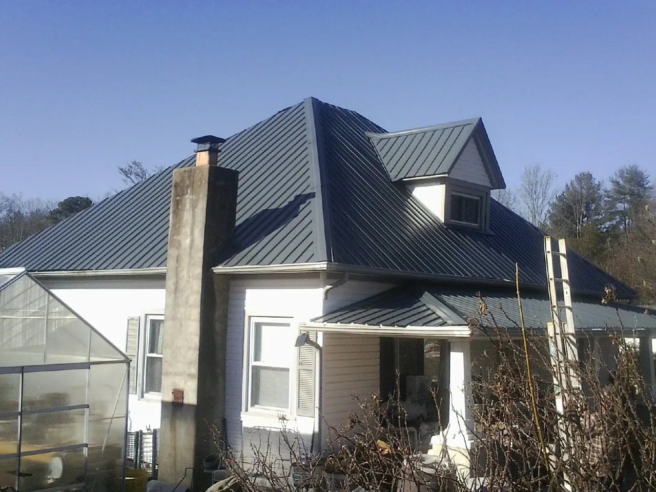 Dark blue standing seam metal roof on a white farmhouse with dormer — Slate & Tile Roof Repair by Roofing Brothers in Towaco