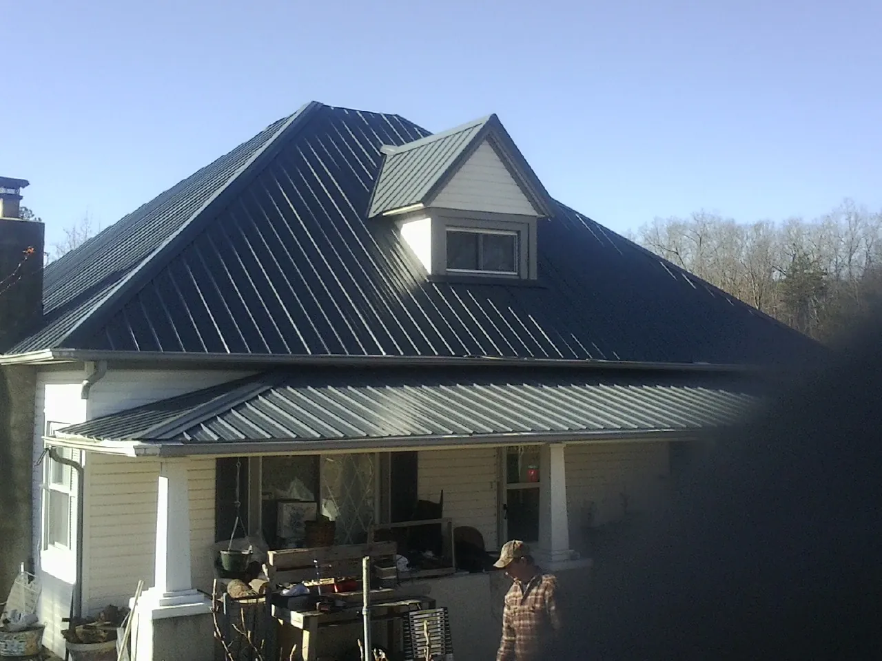 Dark blue standing seam metal roof with a dormer above a front porch in Towaco
