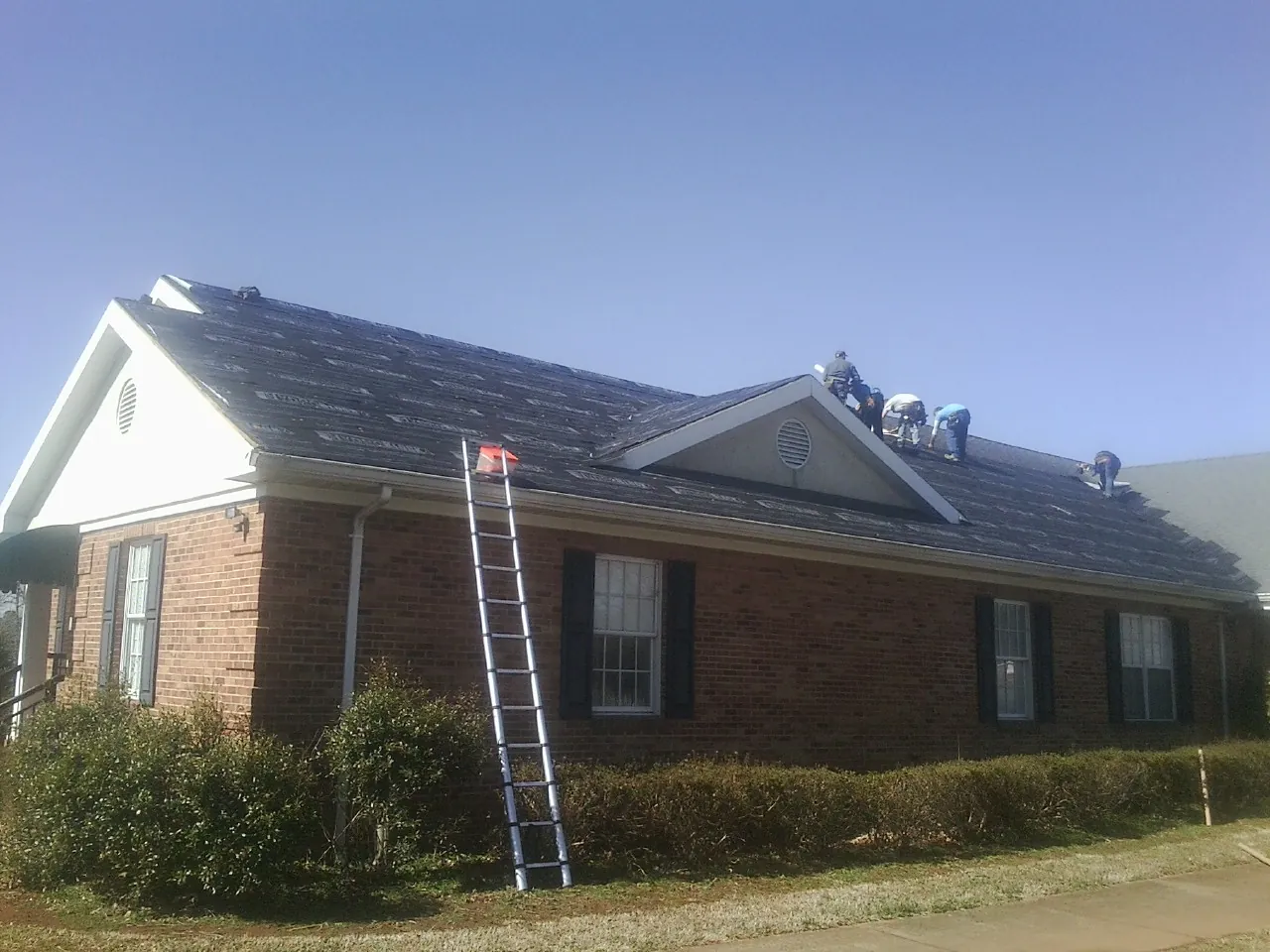 Crew tearing shingles off a brick ranch roof with a ladder set — Emergency Roof Repair work by our crew in Towaco