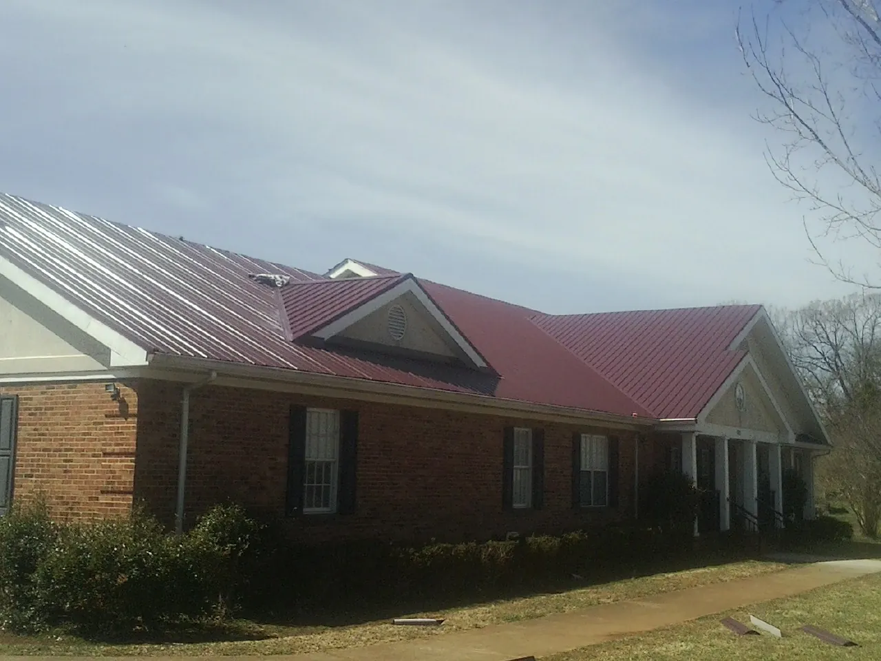 Red metal roof with gabled entries on a long brick building, from a Hail Damage Roof Repair job in Towaco