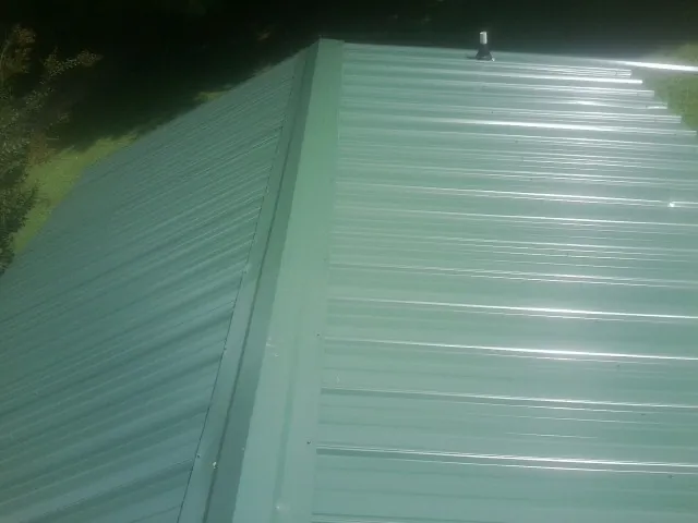 New green metal panels meeting at the ridge of a roof — Flat Roof Repair work by our crew in Towaco
