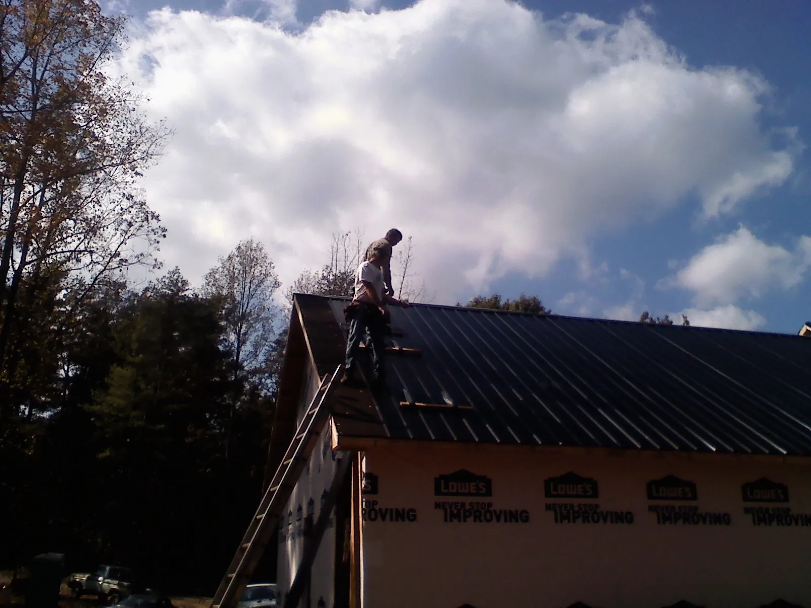 Roofer fastening dark metal panels high against a cloudy sky, from a Roof Inspection job in Towaco